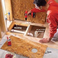 a man in an orange shirt is working on a hole in the floor with tools