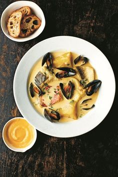 a bowl of soup with mussels and bread on the side