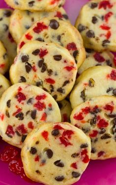 chocolate chip cookies with red and black toppings on a pink plate next to strawberries