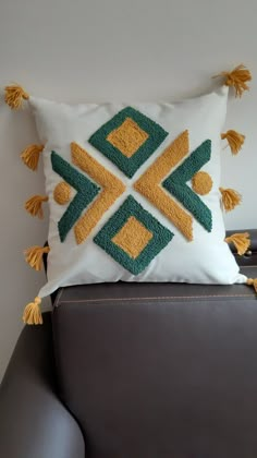 a decorative pillow with tassels on it sitting on a leather chair in front of a white wall