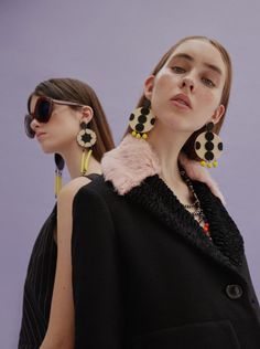 two models in black and white outfits with polka dot earrings on their ears, one wearing a pink fur collar