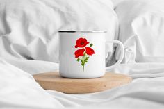 a white coffee mug with red flowers on it sitting on a wooden tray in bed