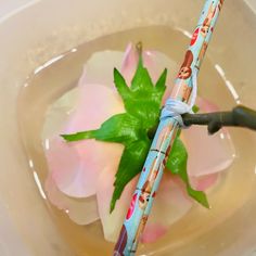 a pair of scissors in a bowl of water with flowers on the side and green leaves