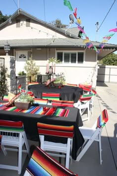 an outdoor dining area with tables and chairs covered in black tablecloths, decorated with colorful streamers