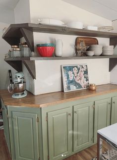 a kitchen with green cabinets and shelves filled with dishes