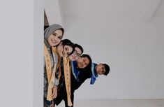 four people posing for the camera in front of a white wall