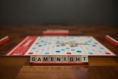 the word game night spelled with scrabble letters on a wooden table next to two red and white dominos