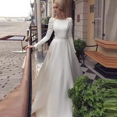 a woman in a long white dress is standing on a balcony next to a bench