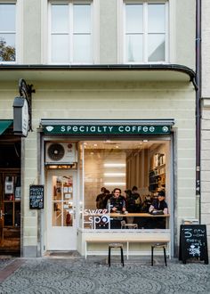 people sitting at tables in front of a specialty coffee shop on the sidewalk outside an apartment building