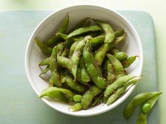 a white bowl filled with green beans on top of a blue tablecloth next to two peas