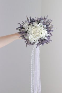 a bridal bouquet with white and purple flowers is held by someone's hand