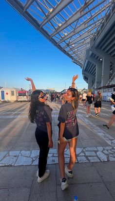 two women are standing on the sidewalk with their arms in the air