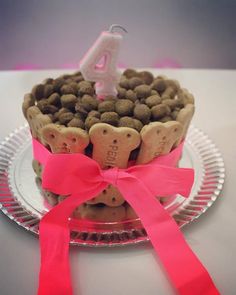 a birthday cake made out of dog biscuits with pink ribbon and candle in the shape of a heart