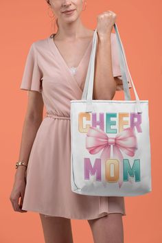 Elevate your game day essentials with our "Cheer Mom" 📣 Canvas Tote Bag! Perfect for proud cheerleader moms, this durable, eco-friendly tote showcases a vibrant, large pink bow 🎀 and colorful letters "Cheer Mom" print on both sides, embodying the spirit of cheerleading with style and convenience. Crafted to carry all your necessities, from pom-poms to snacks, its spacious interior and sturdy handles make it your go-to bag for every cheer event and beyond.  Available in 3 sizes to add both functionality and style, these custom-printed tote bags come with multiple handle colors to match your designs. Made with spun polyester, these bags feature double-stitched seams, cotton webbing straps, and nonwoven laminate lining for high-end durability.  .: Made with 100% polyester, a medium-weight f Casual Shoulder Bag For Mother's Day, White Canvas Shoulder Bag For Mother's Day, Retro White Bags With Letter Print, Retro White Bag With Letter Print, White Canvas Bag For School, White Shoulder Bag With Letter Print For Mother's Day, Fun White Letter Print Bag, Cheer Competition, Cheerleading Mom