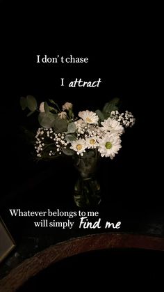 a vase filled with white flowers sitting on top of a table next to a black background