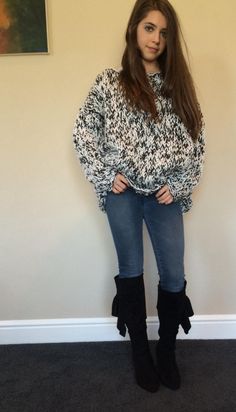 a woman standing in front of a wall wearing boots and a sweater with an animal print on it