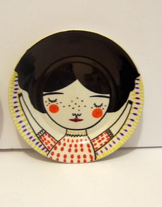 two plates with designs on them are sitting on a table next to each other and one has an image of a woman's face painted on it