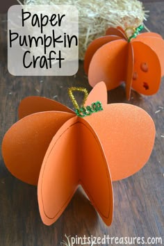 two paper pumpkins sitting on top of a wooden table next to hay and straw