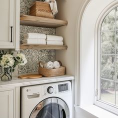 a washer and dryer in a white laundry room with open shelving on the wall