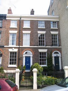 two cars parked in front of a brick building with white trim and windows on the second floor