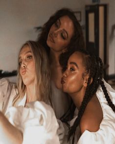 three women are sitting on a bed and one is taking a selfie