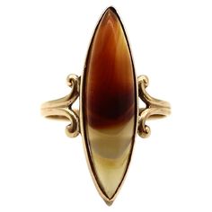 A skinny marquise-shaped banded agate from the Great Northwest decorates the top of this elegant turn-of-the-century ring. The translucent banded agate creates a sliver or boat-like form with its narrow dimensions. The agate is soft to the touch and features creamy colors, brown spots, and a hazy orange color. Together the colors become intertwined and are complimented by the curved motif of the 10k gold band. Circa the 1900’s, this ring is a wonderful antique—a nice piece of history with a cont Colors Brown, Yellow Stone, Brown Spots, Banded Agate, Agate Ring, Gold Band, Antique Rings, 10k Gold, Gold Bands