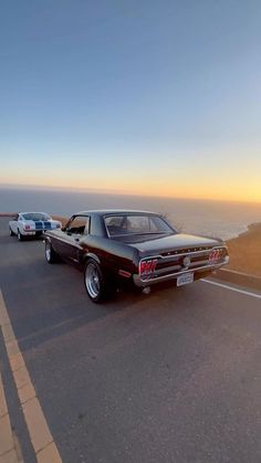 two cars are parked on the side of the road near the ocean at sunset or sunrise