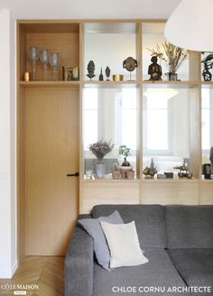 a grey couch sitting in front of a wooden shelf filled with vases and plants