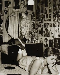 a young woman laying on her bed reading a book and looking at herself in the mirror