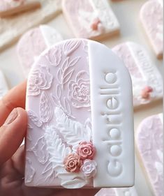 a hand holding a white heart shaped cookie with pink flowers on it's side