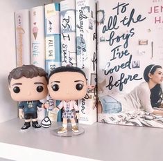 two figurines sitting on top of a book shelf next to a couple of books