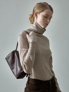 a woman with her eyes closed wearing a turtle neck sweater and carrying a brown bag