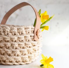 a crocheted basket with yellow flowers in front of it on a white surface