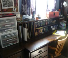 a desk with some drawers and a chair in front of it, next to a window