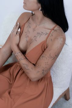 a woman sitting in a chair with tattoos on her chest and arms, looking off to the side