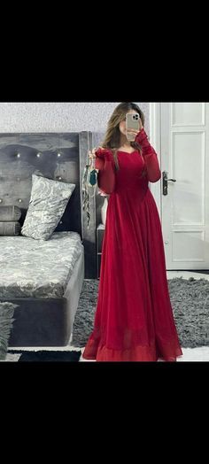 a woman in a red dress taking a selfie with her cell phone while standing next to a bed