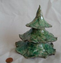 a small green ceramic christmas tree next to a penny