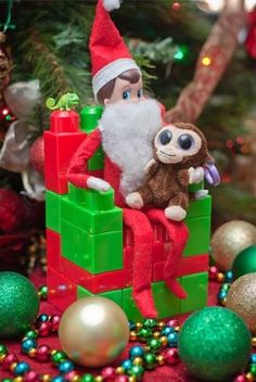 an elf sitting on top of a stack of blocks next to christmas decorations and balls