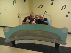 two men and a little boy are sitting on a bed made out of cardboard music notes