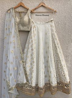 This white and gold threadwork blouse is paired with a multi kali butti lehenga with borders at the hem.  The outfit is completed with a tulle dupatta with a mirror work border and scattered buttis. Threadwork Blouse, Kali Lehenga, Lehenga Simple, Mirror Work Border, Sheer Dupatta, Gold Lehenga, White Lehenga, Indian Outfits Lehenga, Lehnga Dress