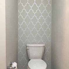 a white toilet sitting in a bathroom next to a wall with a pattern on it