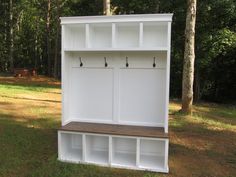 a white bench sitting in the middle of a forest next to some tall trees with hooks on it