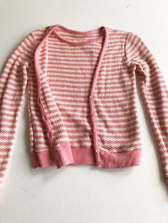 60’s pink/white striped waffle knit sweater has an extra sweater vest panel sewn on the interior, with cardigan construction on the exterior. The sweater has pink knit rib at the sleeve cuffs, hem, neckline, and button placket. The sweater has a button front exterior, but is slip on.ConditionOverall good, has a hole at the left underarm.MeasurementsBust 34”Waist 30”Shoulder 17”Sleeve length 23”Length 21” Pink Crew Neck Cardigan For Layering, Pink Ribbed Winter Cardigan, Pink Ribbed Sweater For Layering, Vintage Sweater For Spring Layering, Pink Ribbed Fitted Cardigan, Fitted Ribbed Pink Cardigan, Pink Fitted Ribbed Cardigan, Retro Ribbed Sweater For Spring, Pink Cotton Sweater For Layering