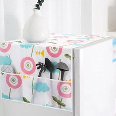 a white vase sitting on top of a refrigerator freezer next to a flowered curtain