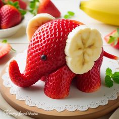 an elephant made out of strawberries and bananas on a plate with other fruit in the background