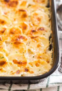 a casserole dish with cheese and meat in it on a towel next to utensils