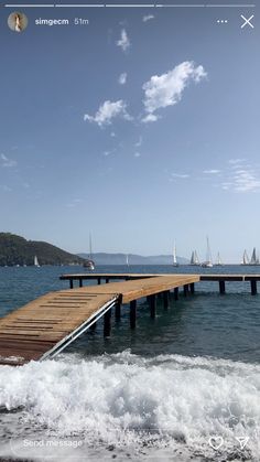 a wooden dock in the ocean with sailboats on the water and blue sky above