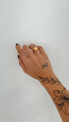 a woman's hand with a gold ring on her left wrist and flower tattoo