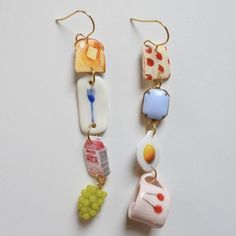 two pairs of earrings with food and drink charms hanging from hooks on a white surface