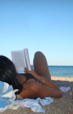 a woman laying on the beach reading a book